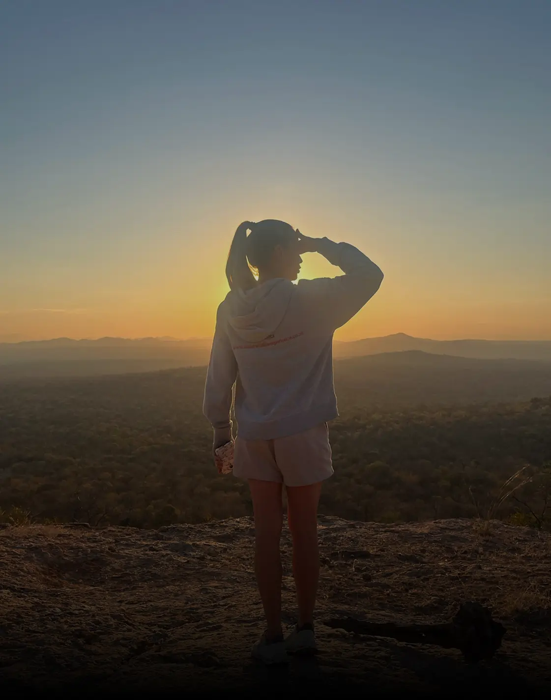 Photo of a volunteer standing in front of a stunning African landscape at sunset